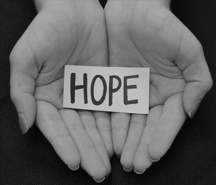 Image shows the palm of hands holding a piece of paper with the word HOPE