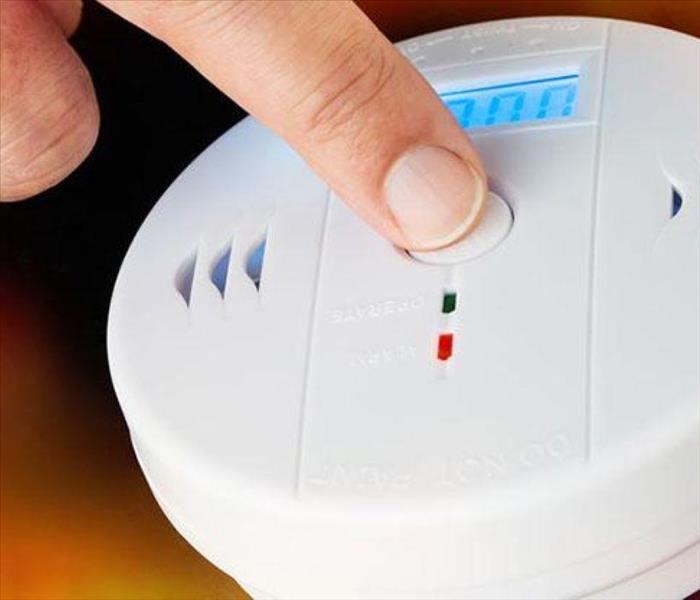 photo of a smoke detector and a pointer finger testing the alarm